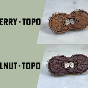 May include: Two wooden dice with a topographic map design. The dice are labeled "20" and are made of cherry and walnut wood.