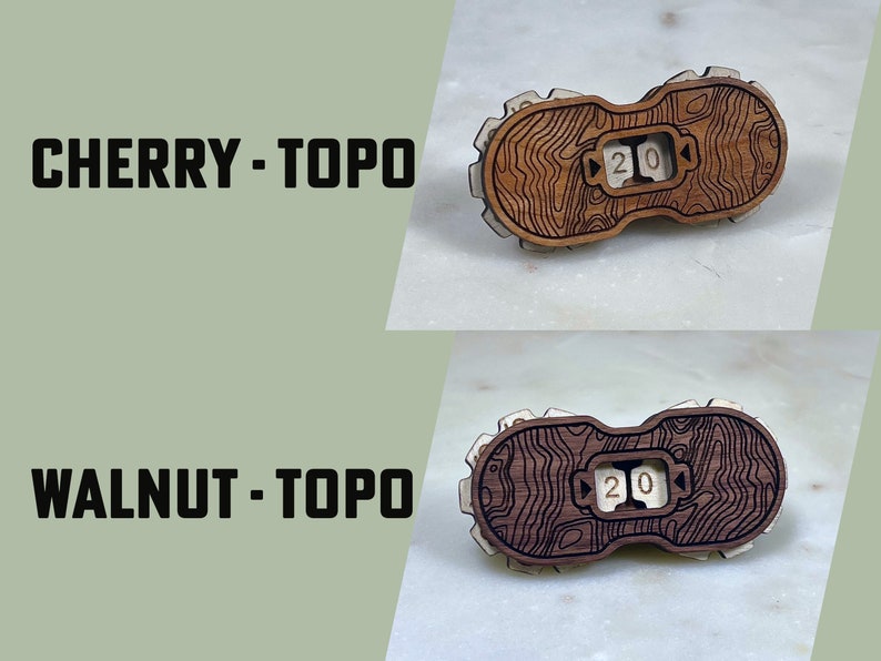 May include: Two wooden dice with a topographic map design. The dice are labeled "20" and are made of cherry and walnut wood.