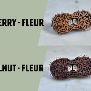May include: Two wooden counter tops with intricate floral designs. The counter tops are labeled "CHERRY - FLEUR" and "WALNUT - FLEUR". Each counter top has a small, white, wooden number "20" displayed in a window.
