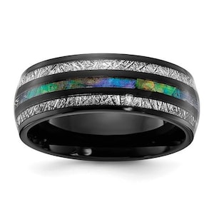 May include: A black ring with a central band of iridescent color and two bands of a textured, silver-colored material. The ring's band is a solid black color, and the iridescent band displays shades of green, blue, and yellow.