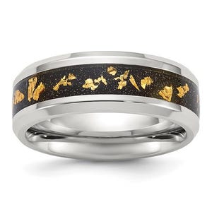 May include: A stainless steel ring with a black inlay featuring gold leaf accents. The ring has a polished finish and a wide band. The gold leaf is scattered throughout the black inlay, creating a striking contrast.