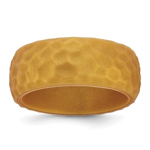Op de afbeelding: Een brede ring met een getextureerde, gehamerde oppervlakteafwerking in een matte goudtint. De ring heeft een consistent, afgerond profiel met een licht onregelmatige, gedeukte buitenstructuur die het licht over het gehele oppervlak opvangt.