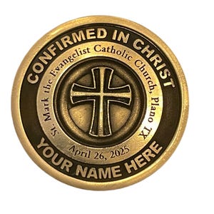 May include: Gold-colored metal coin with the text "CONFIRMED IN CHRIST" around the edge. The center of the coin features a cross with a black outline and a green background. The text "St. Mark the Evangelist Catholic Church, Plano TX" is inscribed around the cross. The date "April 26, 2025" and the text "YOUR NAME HERE" are also inscribed on the coin.