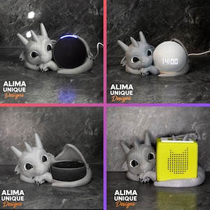 Peut inclure: Un support de haut-parleur en forme de dragon gris avec le texte "ALIMA UNIQUE Designs". Le dragon tient un haut-parleur noir. Le support est conçu pour accueillir le haut-parleur, améliorant son attrait esthétique.