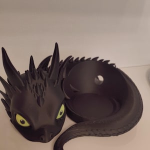 Può includere: Porta bicchiere a forma di drago nero con occhi verdi. Il drago è rannicchiato con la coda avvolta attorno al suo corpo.