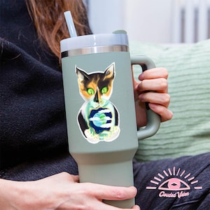 Può includere: Una tazza da viaggio in acciaio inossidabile con un coperchio e un manico verdi. Uno sticker di un gatto calico che tiene un pianeta Terra è sulla tazza.
