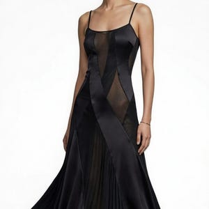 May include: A black evening gown with spaghetti straps and a flowing skirt. The dress features sheer panels and diagonal satin accents, creating a sophisticated and elegant silhouette. The skirt has a pleated design.