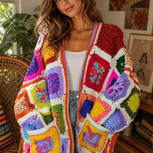 May include: A vibrant, handmade crochet cardigan in a patchwork design. The colorful garment features squares of red, orange, yellow, green, purple, and blue, with white borders and pockets. The cardigan is open-fronted and has long sleeves.