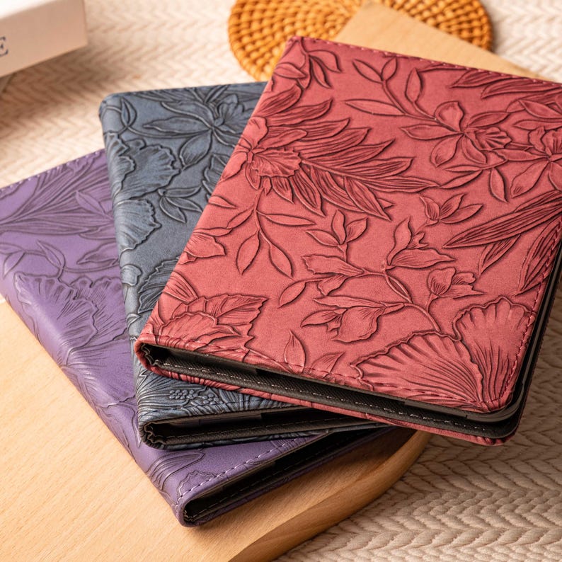 May include: Three different patterned book covers. The top cover is red with a floral design. The middle cover is dark blue with a floral design. The bottom cover is purple with a floral design.