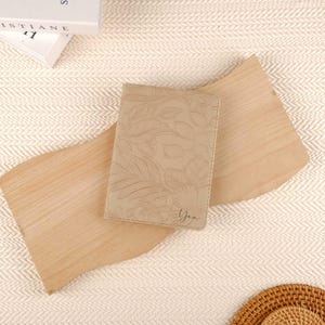 May include: A beige leather passport holder with a floral embossed design. The holder has the name "Yan" embossed on the front.