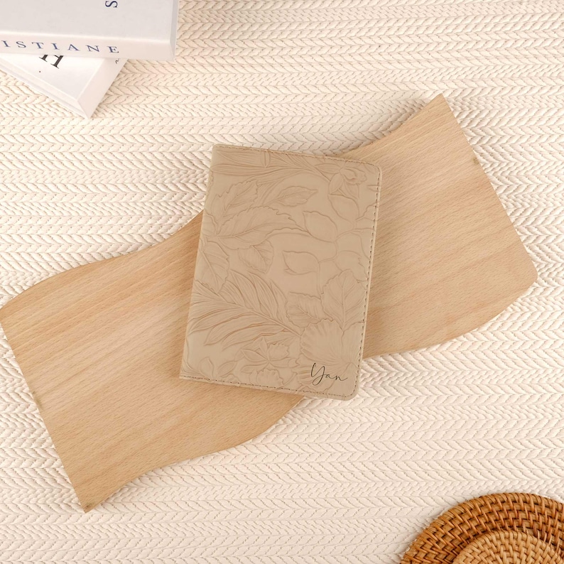 May include: A beige leather passport holder with a floral embossed design. The holder has the name "Yan" embossed on the front.