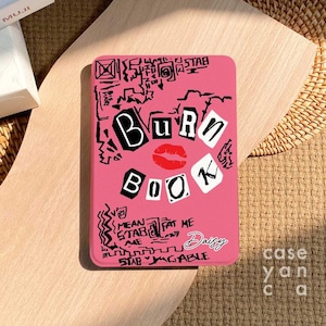 May include: Pink notebook with the words "Burn Book" in black letters. The notebook has black and white doodles and text, including "Mean Girls" and "Daisy".
