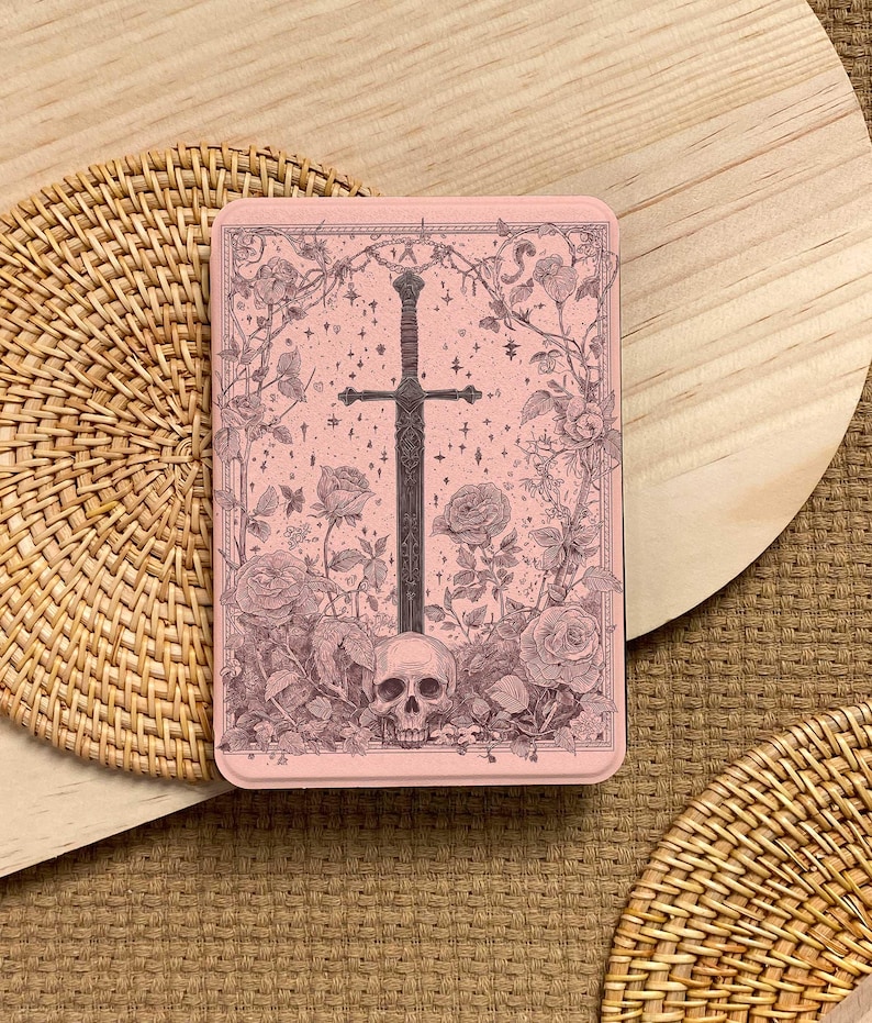Peut inclure: Une bo&icirc;te rectangulaire rose avec une illustration d&eacute;taill&eacute;e d'une &eacute;p&eacute;e, de roses, d'un cr&acirc;ne et d'&eacute;toiles. L'&oelig;uvre d'art est de style vintage, avec une &eacute;p&eacute;e sombre au centre et des &eacute;l&eacute;ments floraux. La bo&icirc;te est pos&eacute;e sur une surface en bois.
