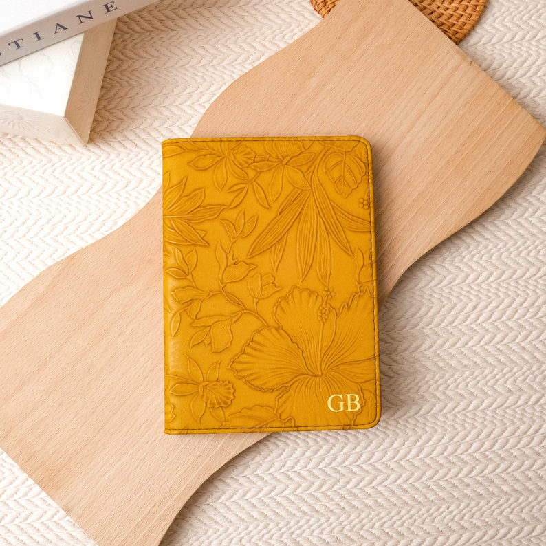 May include: A yellow leather passport holder with a floral embossed design and the initials "GB" in gold lettering.