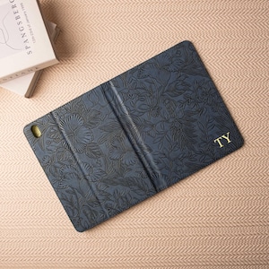 May include: A blue floral patterned iPad case with a gold monogram "TY" on the back.