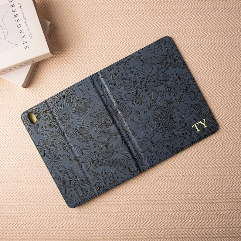 May include: A blue floral patterned iPad case with a gold monogram "TY" on the back.