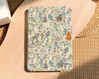 May include: A beige tablet case featuring a whimsical floral and animal pattern. The design includes illustrations of deer, foxes, rabbits, and other woodland creatures amidst colorful flowers. The name "Daisy" is written in cursive.