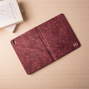 May include: A burgundy leather iPad case with a floral pattern and the initials "FG" embossed on the back.