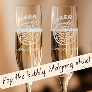 May include: Two champagne flutes filled with bubbly, featuring etched designs and names. The flutes have a "JOKER" design and a Mahjong-style graphic. The text "Pop the bubbly, Mahjong style!" is also present.