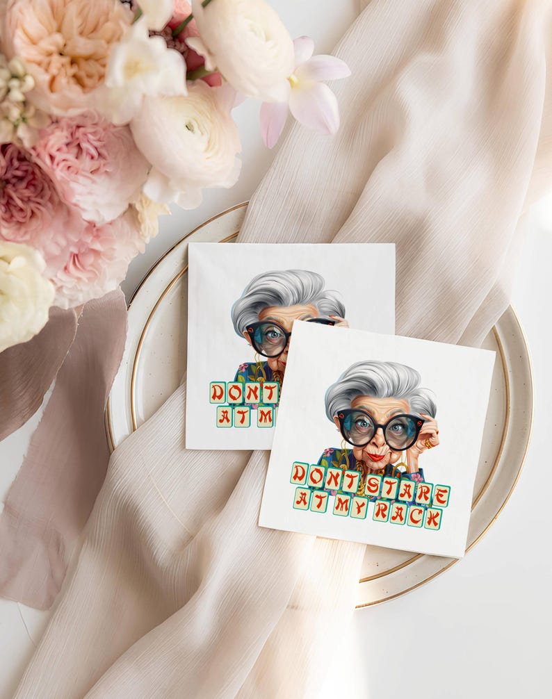 Op de afbeelding: Twee vierkante witte servetten met een kleurrijke illustratie van een vrouw met een grote bril en de tekst "DON'T STARE AT MY RACK". De servetten liggen op een witte plaat met een gouden rand, met bloemen en een beige doek op de achtergrond.