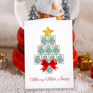 May include: A white greeting card with a Christmas tree design made of Joker playing cards, topped with a gold star and a red bow. The text "Merry Mah Jongg" is written in red script at the bottom.