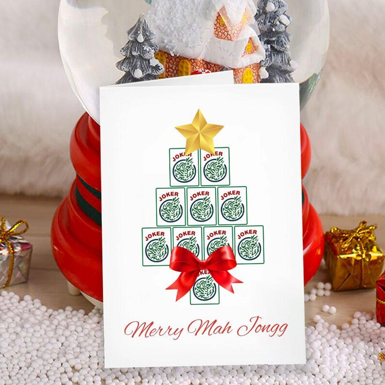 May include: A white greeting card with a Christmas tree design made of Joker playing cards, topped with a gold star and a red bow. The text "Merry Mah Jongg" is written in red script at the bottom.