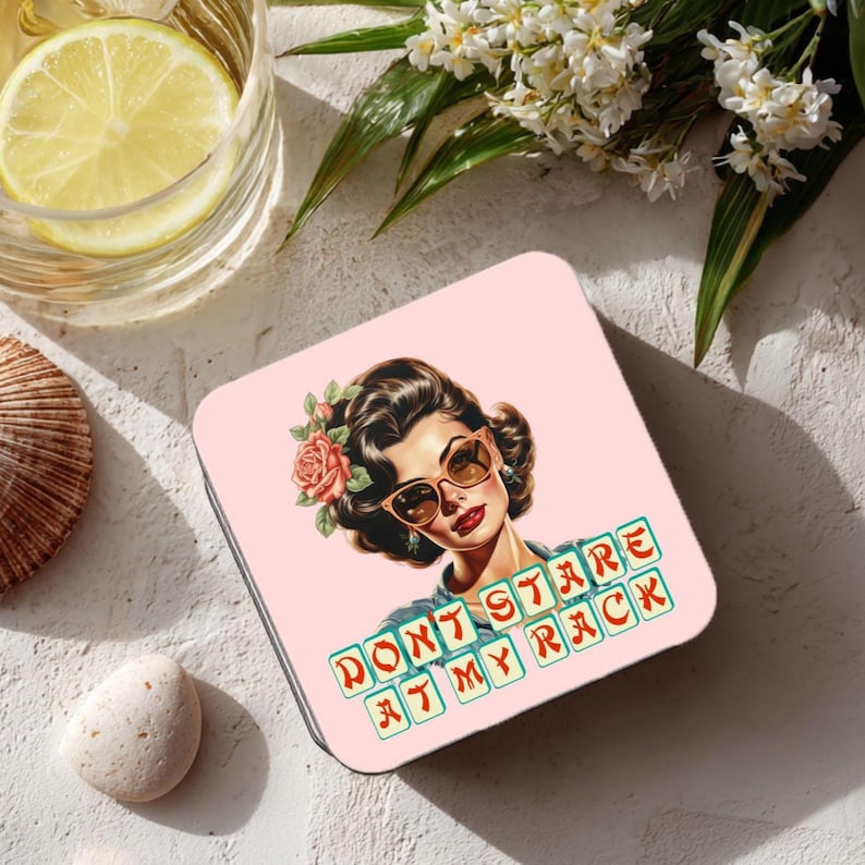 May include: Square pink coaster featuring a vintage illustration of a woman with sunglasses and a rose in her hair. The coaster has the text "DON'T STARE AT MY RACK" in a retro font.