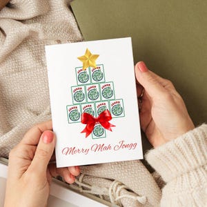 May include: A white greeting card with a Christmas tree design made of playing cards that say "Joker". The tree is topped with a gold star and a red bow. The text "Merry Mah Jongg" is written in red.