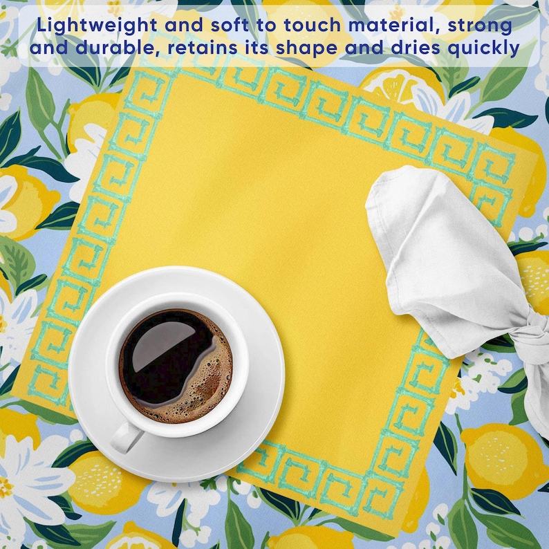 Puede incluir: Un mantel individual amarillo con un borde turquesa y una servilleta blanca. Una taza y un platillo blancos con caf&eacute; oscuro est&aacute;n en el mantel individual. El fondo es un estampado floral azul con limones. El texto dice: Material ligero y suave al tacto, fuerte y duradero, conserva su forma y se seca r&aacute;pidamente.