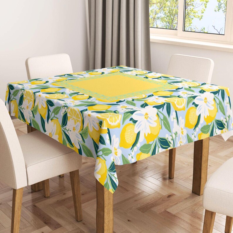 Puede incluir: Un mantel rectangular con un dise&ntilde;o de limones y flores. El dise&ntilde;o incluye limones amarillos, flores blancas y hojas verdes sobre un fondo azul claro. Un cuadrado amarillo est&aacute; en el centro, con un borde verde. El mantel est&aacute; sobre una mesa de madera.