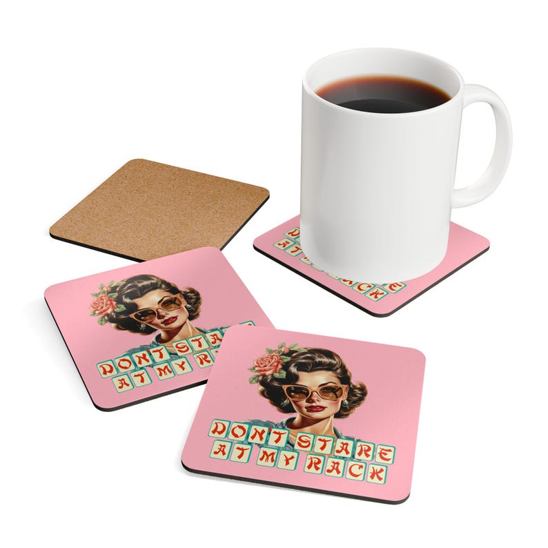 May include: A white ceramic mug filled with coffee sits on a pink coaster with a retro illustration of a woman wearing sunglasses and the text "DON'T STARE AT MY RACK". Additional coasters are visible.