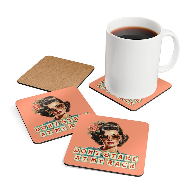 May include: A white ceramic mug filled with dark liquid sits on a square coaster. The coaster and two others feature a retro illustration of a woman wearing sunglasses and the text "DON'T STARE AT MY RACK". A fourth coaster is made of cork.