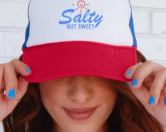 May include: A red, white, and blue trucker hat with the text "Salty but Sweet" in blue script. The hat has a white front panel, a red brim, and a blue mesh back. A smiling sun graphic is above the text.