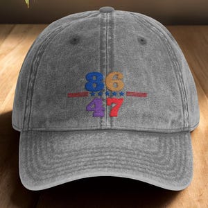 May include: Charcoal grey baseball cap with embroidered colorful numbers 86 and 47, separated by a red line and stars. The hat is made of a soft, worn fabric and has a curved brim. The text "Charcoal Grey" is in the top right corner.