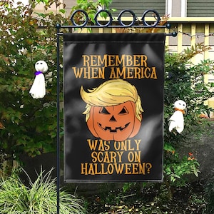 Puede incluir: Bandera de jard&iacute;n negra de Halloween con el texto "REMEMBER WHEN AMERICA WAS ONLY SCARY ON HALLOWEEN?" y una calabaza con pelo rubio. Dos peque&ntilde;as decoraciones de fantasmas a cada lado.