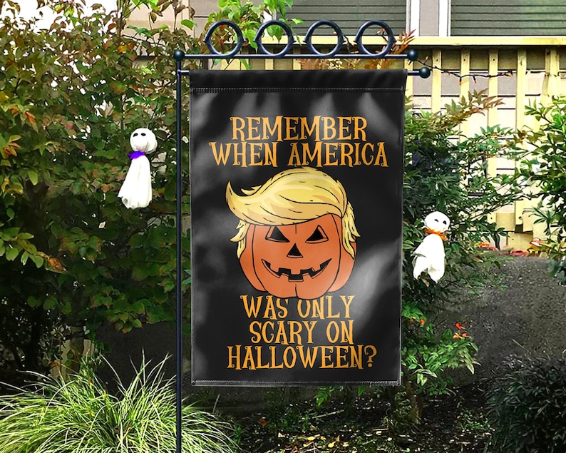 Puede incluir: Bandera de jard&iacute;n negra de Halloween con el texto "REMEMBER WHEN AMERICA WAS ONLY SCARY ON HALLOWEEN?" y una calabaza con pelo rubio. Dos peque&ntilde;as decoraciones de fantasmas a cada lado.