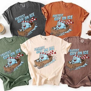 May include: Several t-shirts in different colours, each displaying the text "Fastest Guy on Ice" above a cartoon ice cube character on a sled. The shirts are in shades of grey, orange, green, beige, and brown.