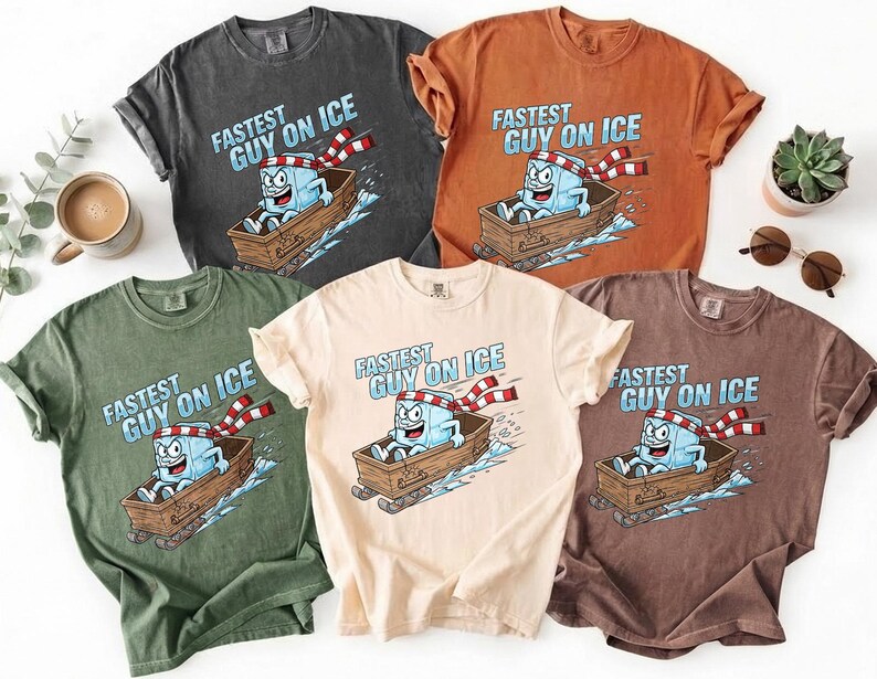 May include: Several t-shirts in different colours, each displaying the text "Fastest Guy on Ice" above a cartoon ice cube character on a sled. The shirts are in shades of grey, orange, green, beige, and brown.