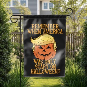 Puede incluir: Bandera de jard&iacute;n negra con el texto "REMEMBER WHEN AMERICA WAS ONLY SCARY ON HALLOWEEN?" y una calabaza con pelo rubio. La bandera est&aacute; colgada de un soporte de metal negro en un jard&iacute;n.