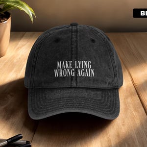 May include: A black baseball cap with a distressed, washed-out finish. The front of the cap features the embroidered white text "MAKE LYING WRONG AGAIN" in a clean, sans-serif font. The cap has a structured crown, a curved brim, and a top button.