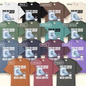 May include: A collection of t-shirts in various colors, including white, black, and blue. Each shirt features the text "EVEN THE FROZEN DEAD GUY" and "NEED COFFEE" with a graphic of a hand emerging from ice and a coffee cup. The shirts are short-sleeved.