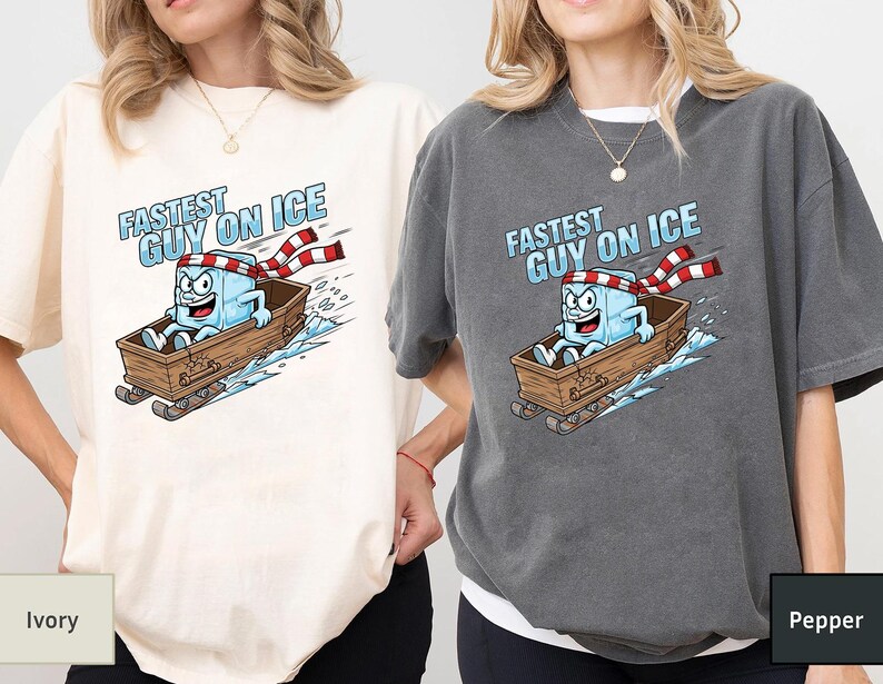 May include: Ivory and pepper-coloured t-shirts with a cartoon ice cube character in a wooden sled, text reads "Fastest Guy on Ice." The ice cube wears a red and white striped scarf and has a determined expression.
