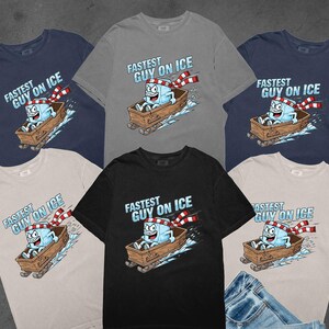 May include: Various t-shirts in navy, grey, black, and beige. Each has a cartoon ice cube sledding, with the text "FASTEST GUY ON ICE" above. The ice cube is wearing a red and white scarf, a fun design for clothing.