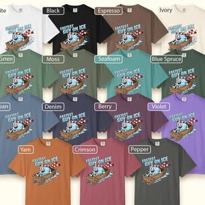 May include: A selection of short-sleeved t-shirts in various colours, each displaying a cartoon design of a character in a boat with the text "FASTEST GUY ON ICE". Colours include white, black, and green.