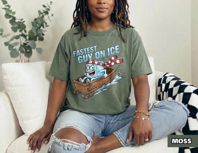 May include: An olive green t-shirt featuring the text "FASTEST GUY ON ICE" and a cartoon ice cube character on a sled. The ice cube wears a red and white scarf. The word "MOSS" is in a green rectangle.