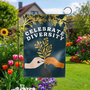 May include: A garden flag with the words "CELEBRATE DIVERSITY" in white on a dark teal background. The flag features gold floral accents and illustrations of hands tending a plant. The flag is displayed in a garden with colorful flowers and greenery.