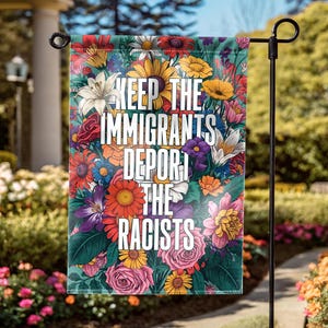 May include: A garden flag with a floral design and the text "KEEP THE IMMIGRANTS DEPORT THE RACISTS" in white. The flag features a variety of flowers in shades of red, yellow, pink, purple, and blue against a teal background.