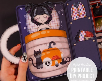 May include: A Halloween-themed paper craft project. The design features a sleeping girl, a pumpkin, a black cat, and a skull. The project also includes a pajama top and a mushroom. The image text reads "Digital Download Printable DIY Project".
