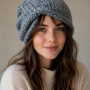 May include: A chunky knit beanie in a heathered grey colour. The hat features a thick, ribbed texture with a slightly slouchy fit and a folded brim. The yarn has a visible, multi-tonal grey appearance, creating a soft and textured look.