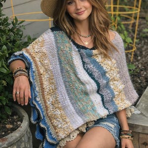 May include: A straw sun hat and a colorful knitted poncho with blue, white, and tan stripes. The poncho has a scalloped edge and is worn over denim shorts. A necklace and bracelets complete the look.